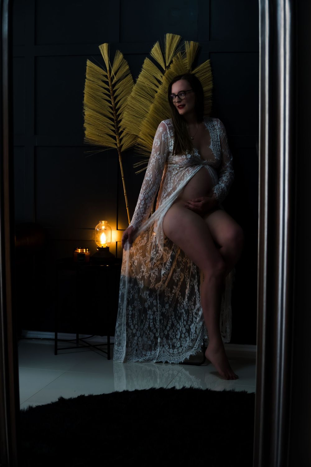 Moody boudoir photography with lace dress and palm fronds in low light setting.