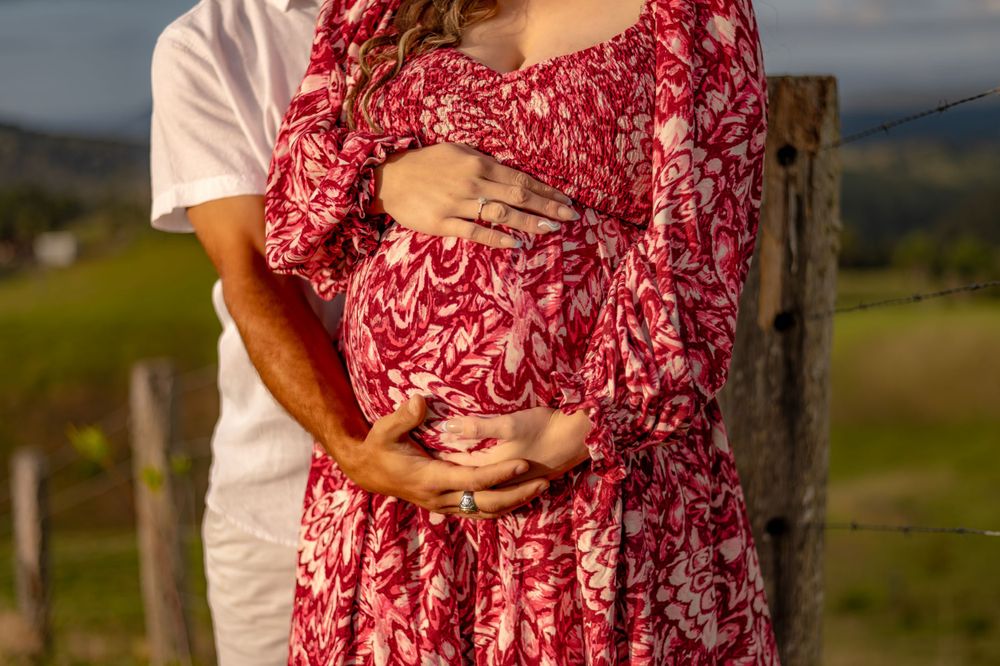 Woman in red floral dress standing in natural outdoor setting.