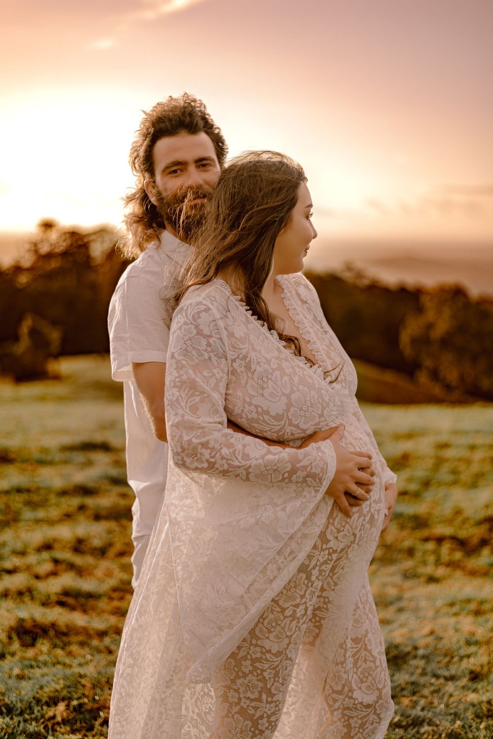 Intimate embrace captured in golden sunset light on grassy hillside.