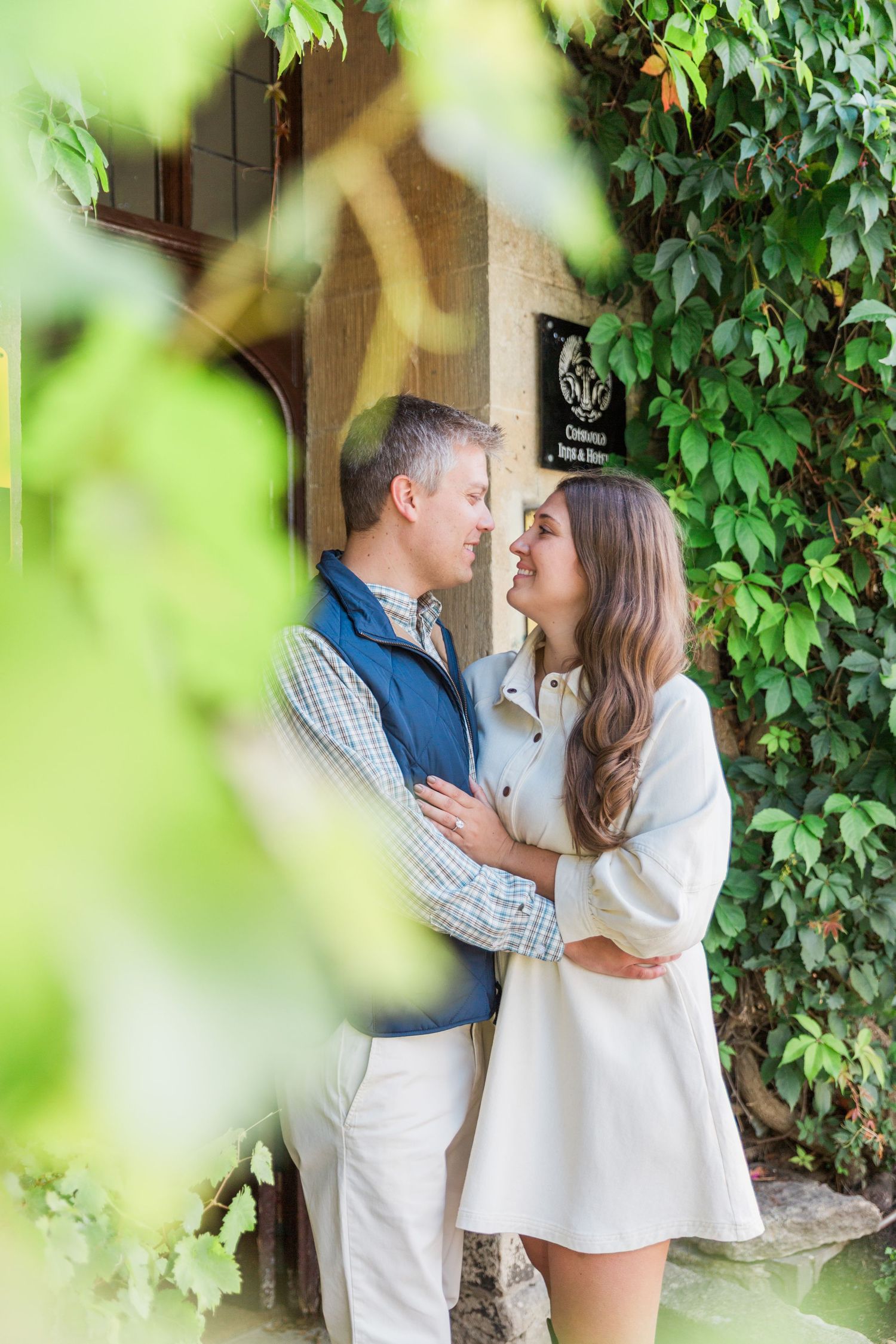 A newly engaged couple embrace outside the swan at Bibury cotswolds. Proposal & Engagement Photography Hayley Elizabeth