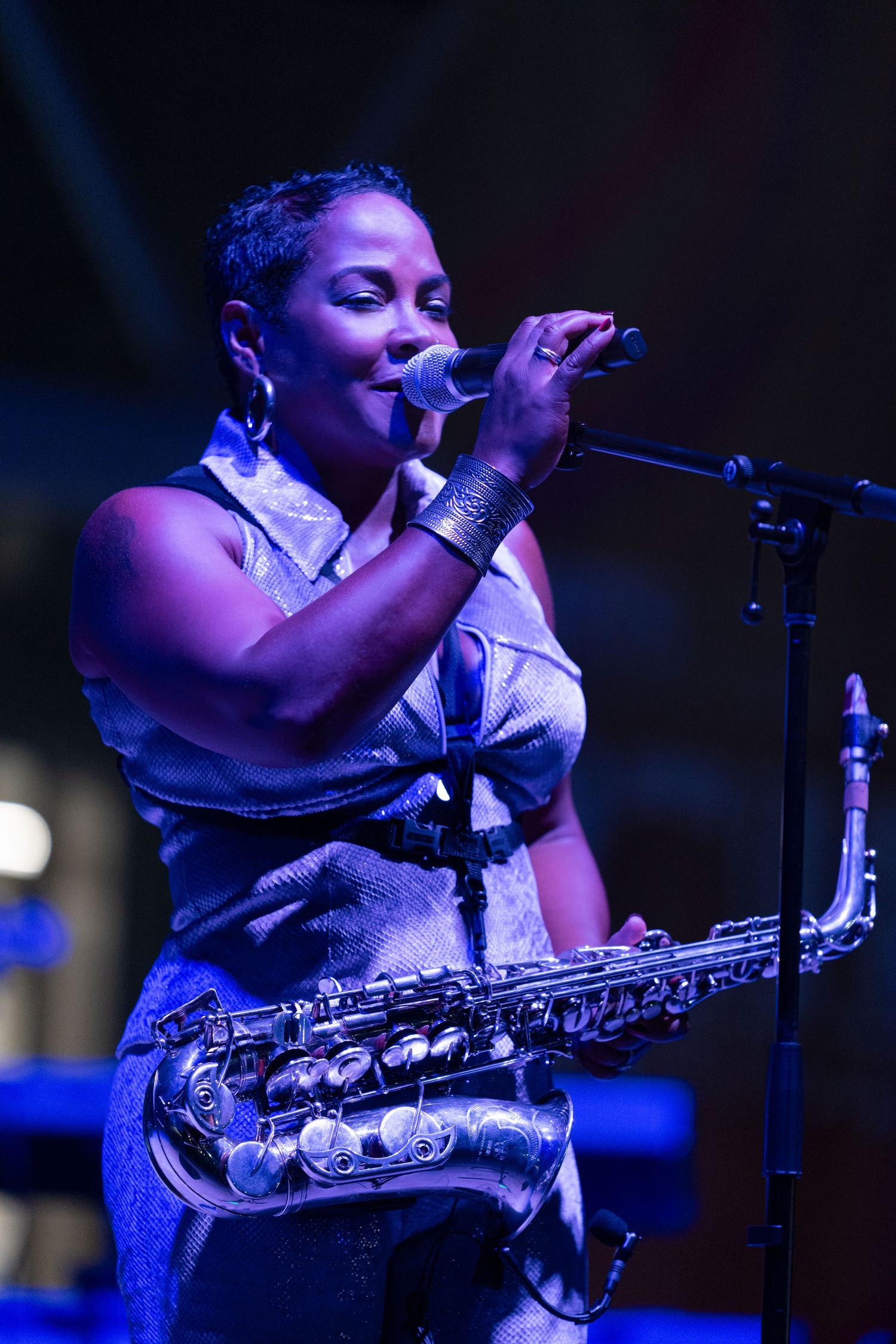 A musician performs on stage with a saxophone under dramatic blue lighting during a concert performance.