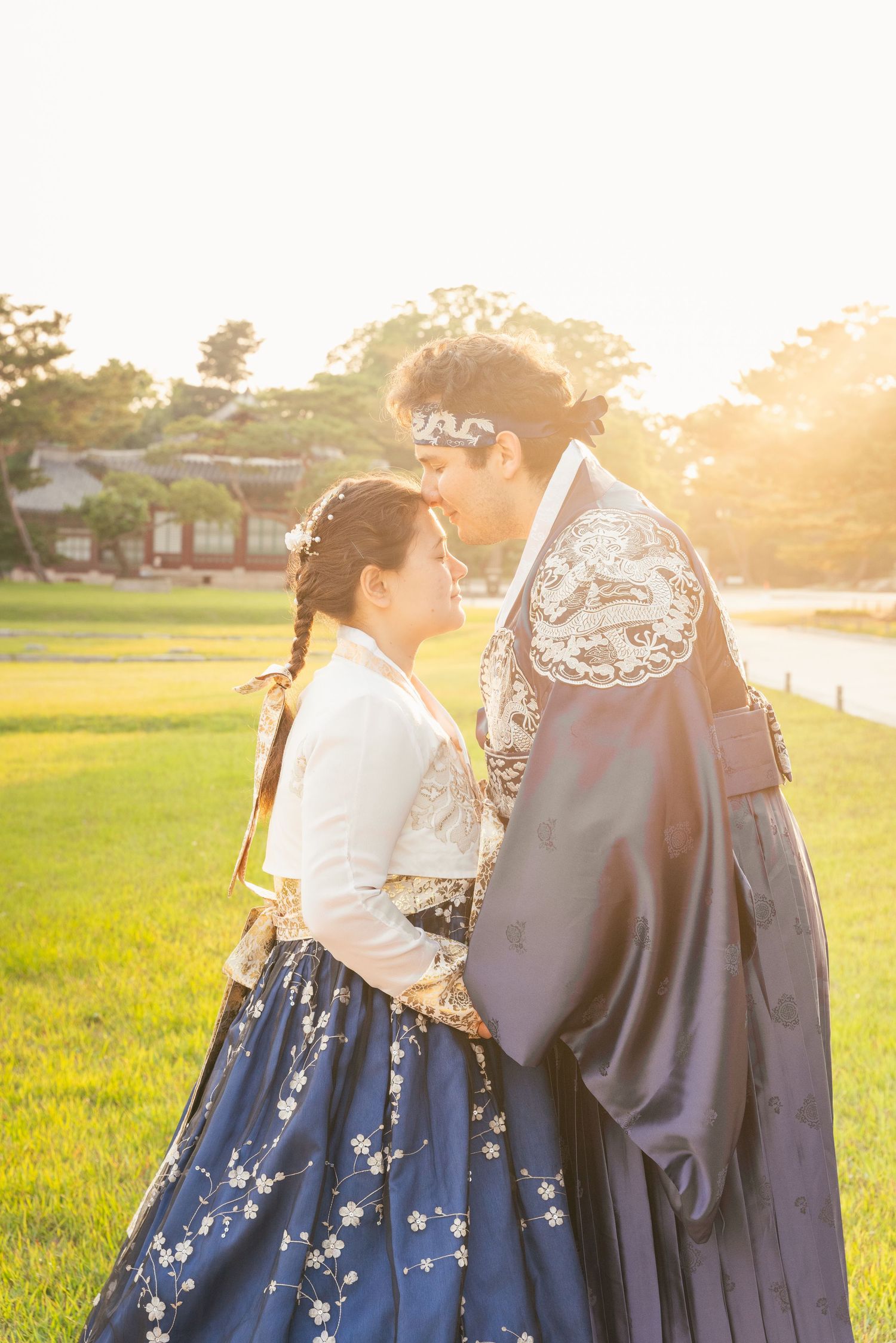 People wearing traditional Korean hanbok clothing pose together at a historic palace courtyard during sunset.