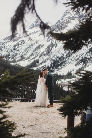A couple shares an intimate moment during their winter mountain wedding with snow-capped peaks providing a majestic backdrop.