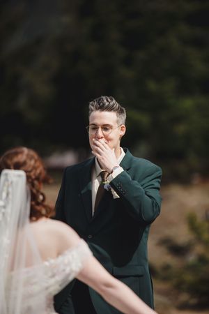 Emotional groom wipes tears from his eyes during first look with bride in wedding ceremony.