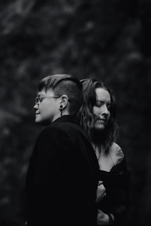 A black and white artistic portrait shows a romantic couple embracing in dark atmospheric lighting.