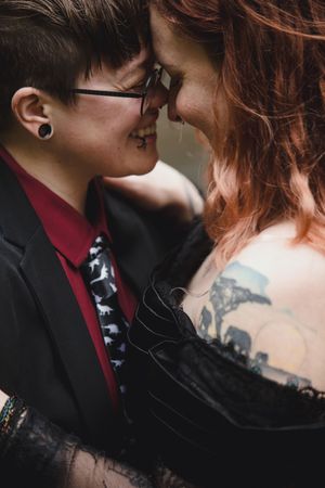 A close intimate moment between a couple with visible tattoos, glasses, and formal attire including a tie and jacket.