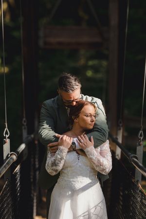 Couple shares intimate moment on swings during outdoor wedding ceremony, with bride wearing delicate lace gown.