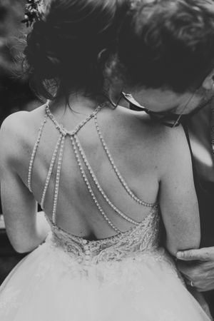 Back view of wedding dress with intricate pearl strands and lace detailing forming a delicate crisscross pattern.