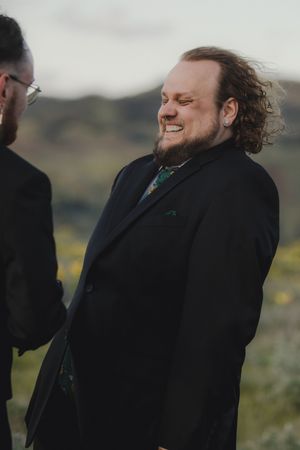 Two people in formal attire laughing and talking together outdoors in a natural setting with muted hills in background.
