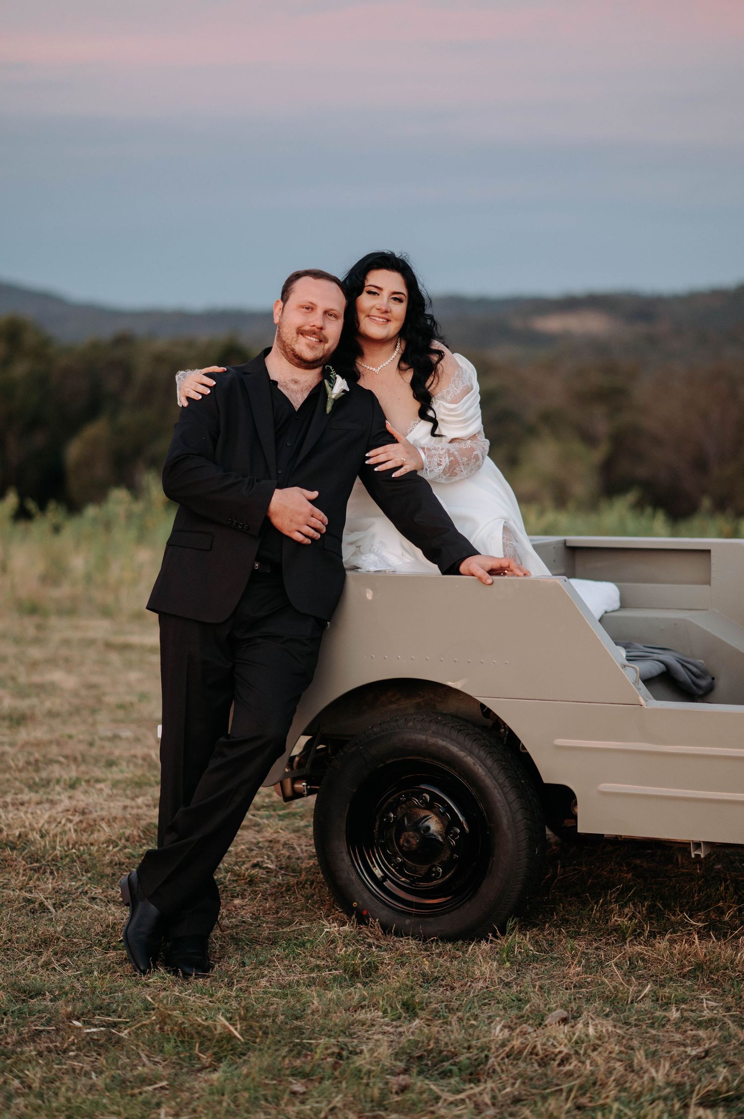 A romantic wedding moment captured through an arched mirror outdoors with mountains in the background.