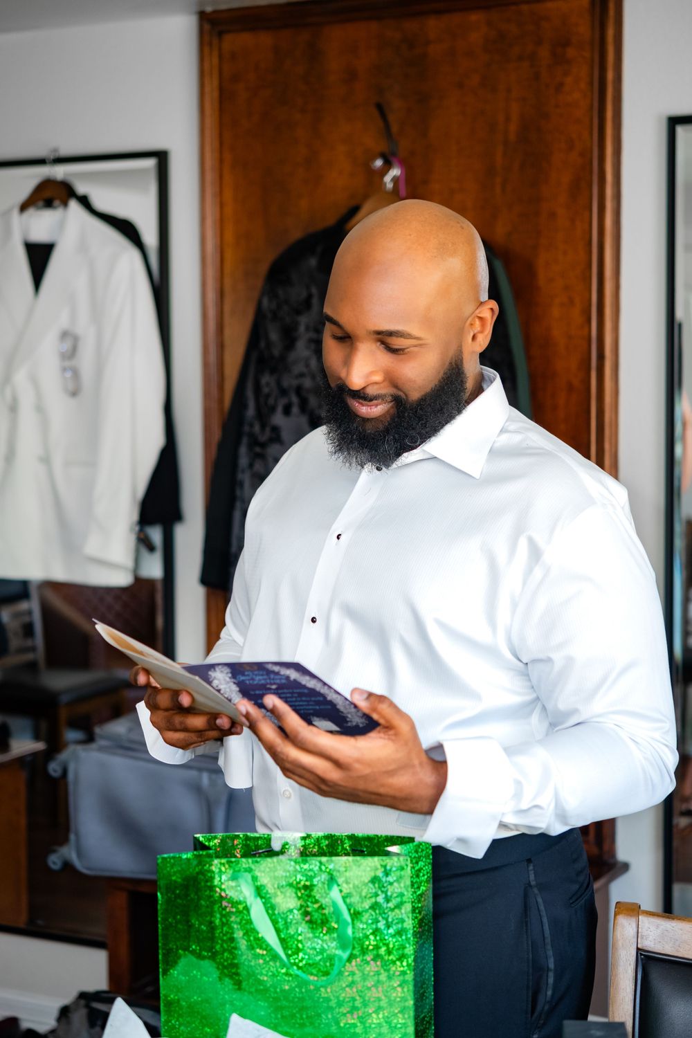 A well-dressed person in a white dress shirt smiles while reading a document next to a bright green shopping bag.