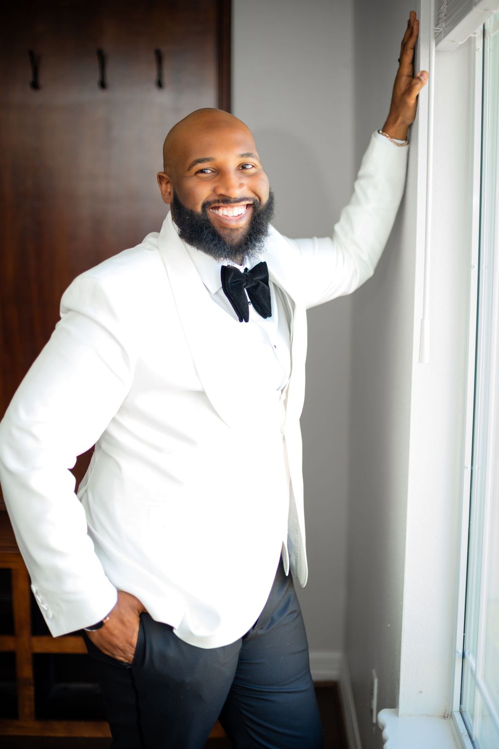 A man in a white dress shirt and dark pants poses confidently by a window in a series of casual portraits.