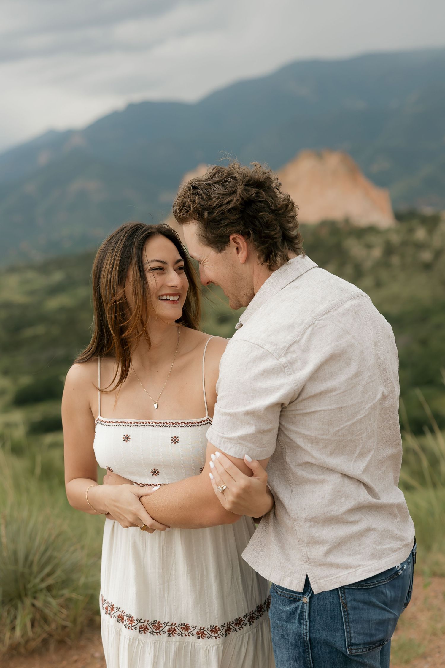 A romantic couple in white outfits share intimate moments against a mountain backdrop at Garden of the Gods.