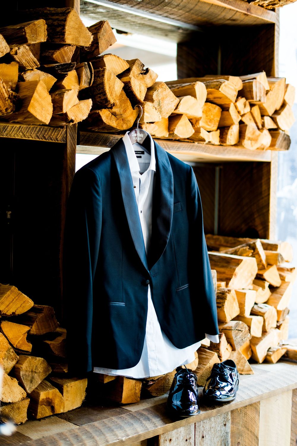 Navy blue suit jacket and dress shoes displayed against rustic wood pile background.