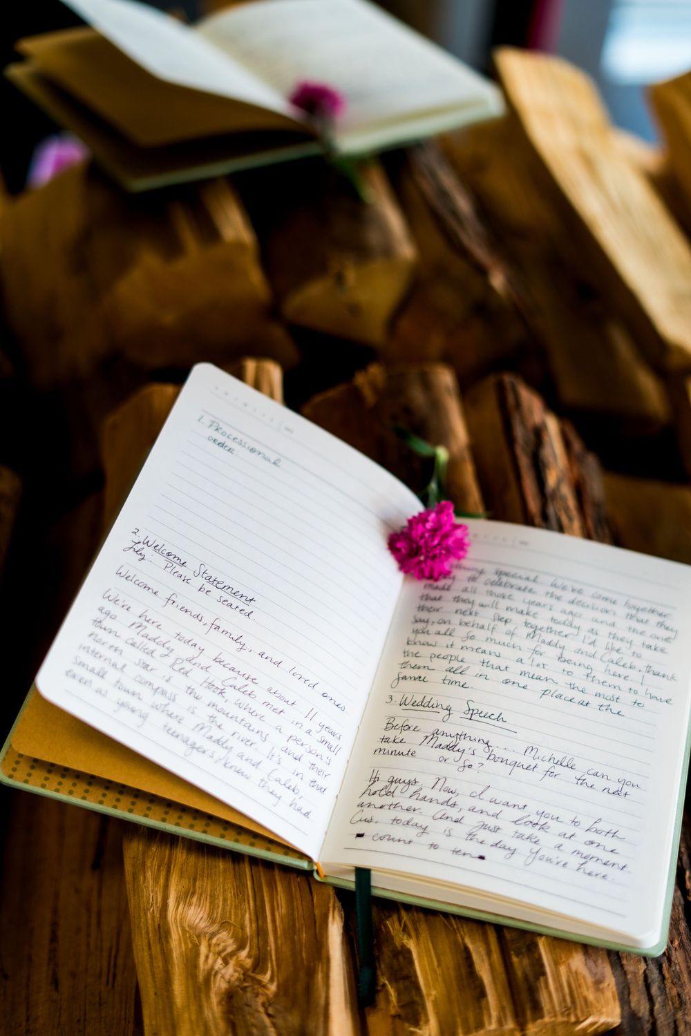 Handwritten wedding guest book pages with pink flower decoration on rustic wooden surface.
