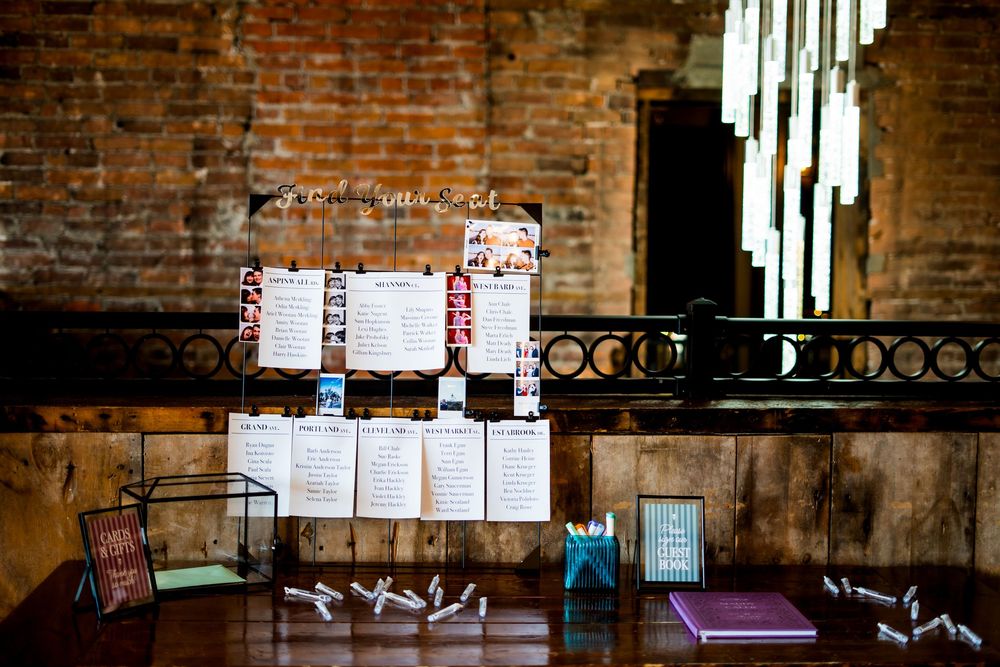 Wedding seating charts displayed on exposed brick wall with hanging lights.