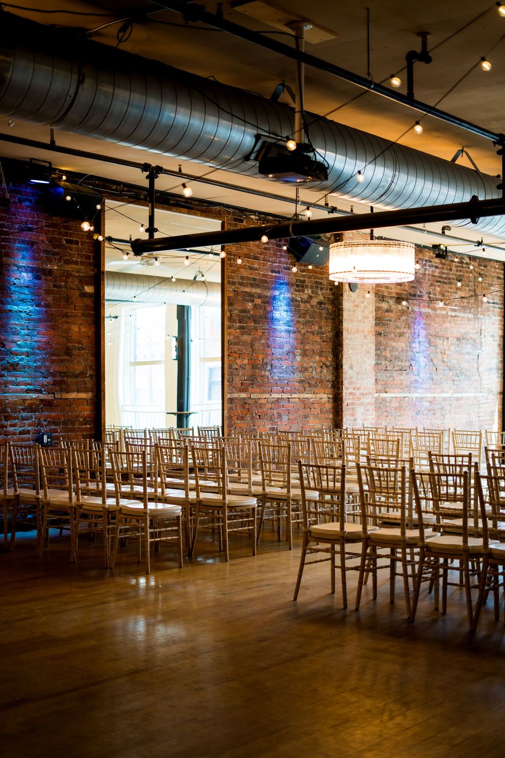 Industrial wedding venue with exposed brick walls and gold chiavari chairs set up for ceremony.