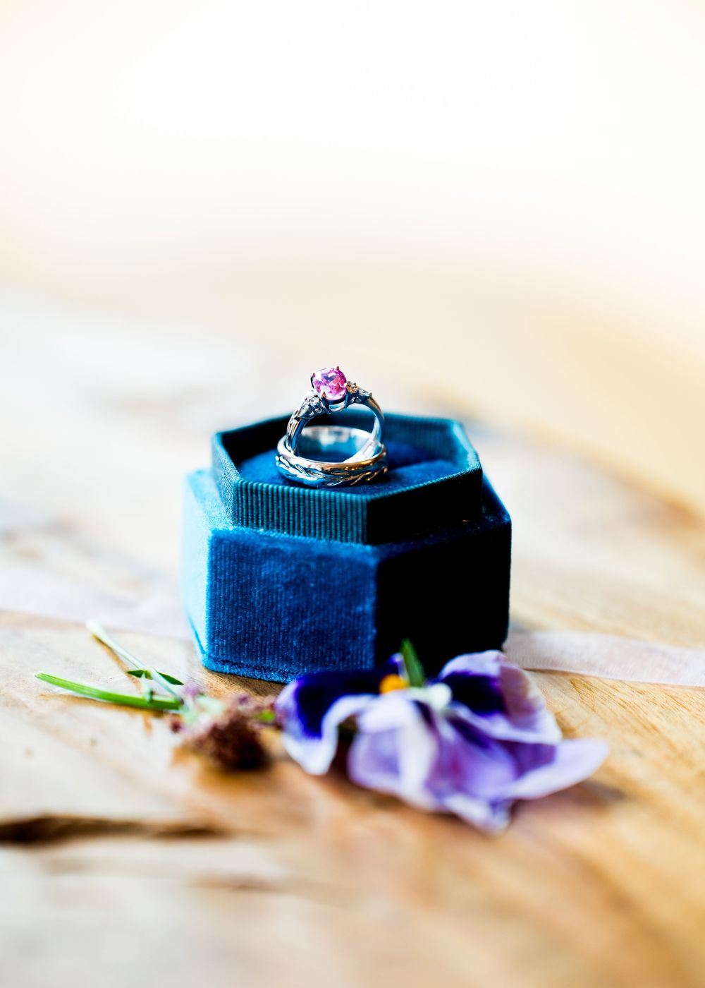 Close-up sequence of wedding rings and purple flowers arranged on a wooden surface.