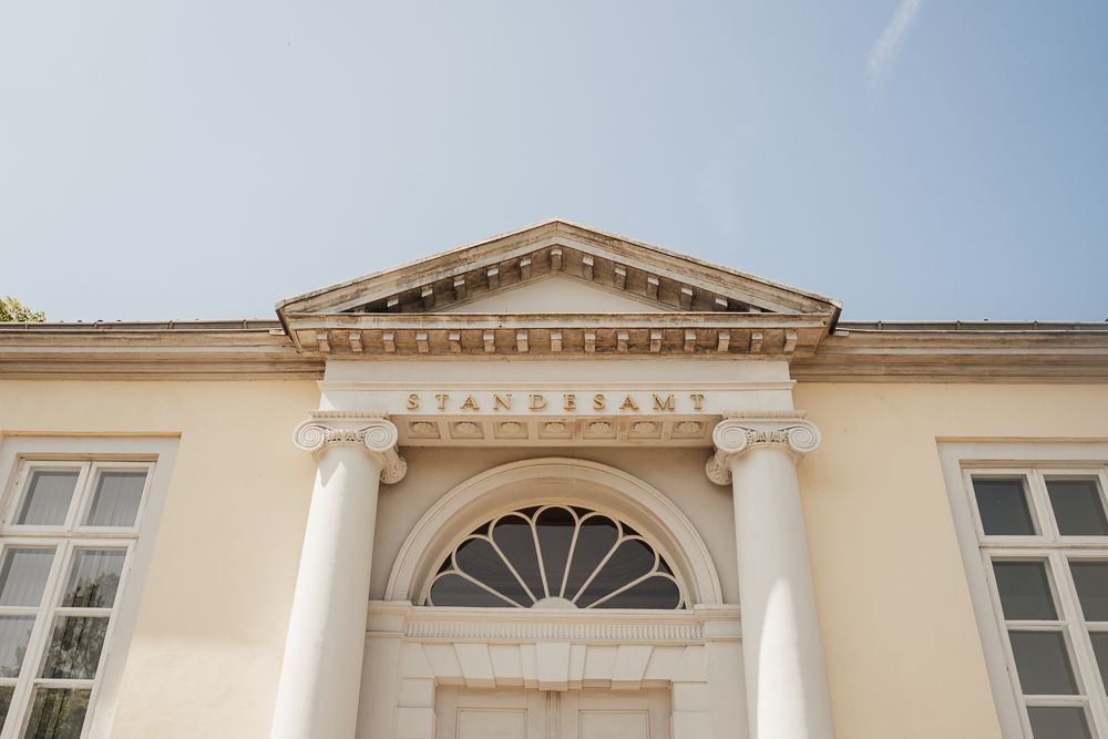 Elegant white neoclassical building exterior with ornate architectural details and arched windows along the facade.