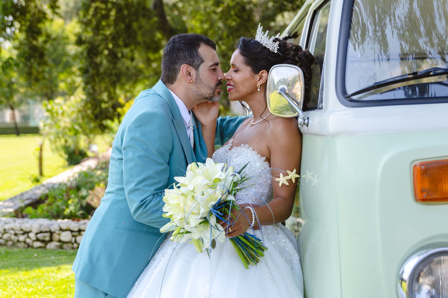 Classic mint green VW bus serves as backdrop for wedding photos in a sunny garden setting.