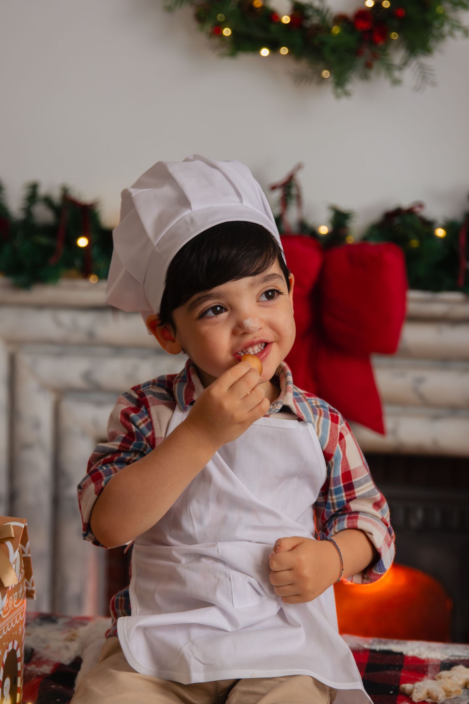 Toddler in white cap and plaid shirt giggling during Christmas photo session.
