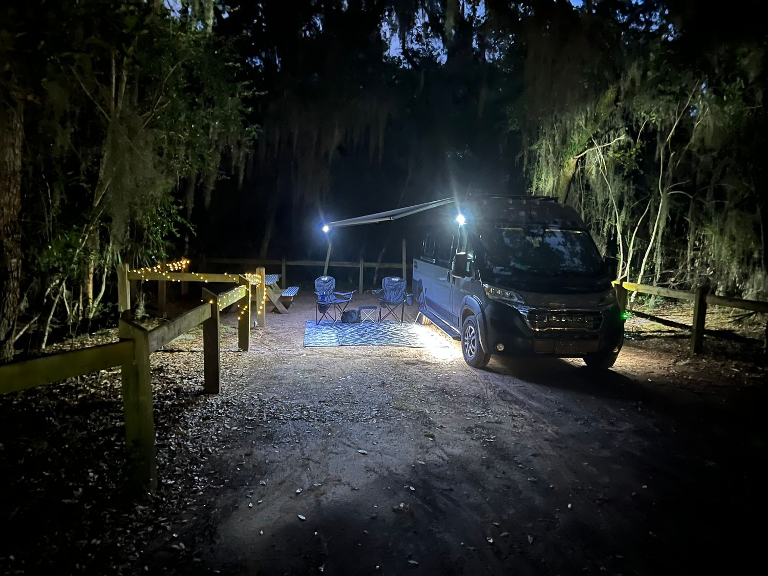 Van parked at a dark wooded campsite illuminated by bright lights at night in Florida.