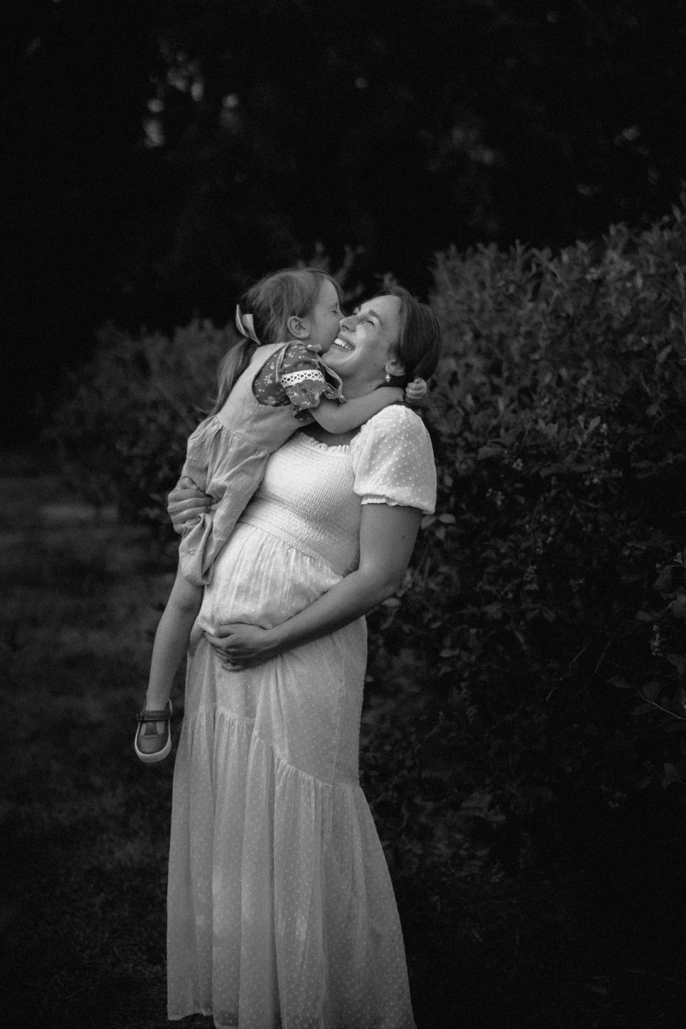 Black and white portrait of mother and child embracing outdoors.