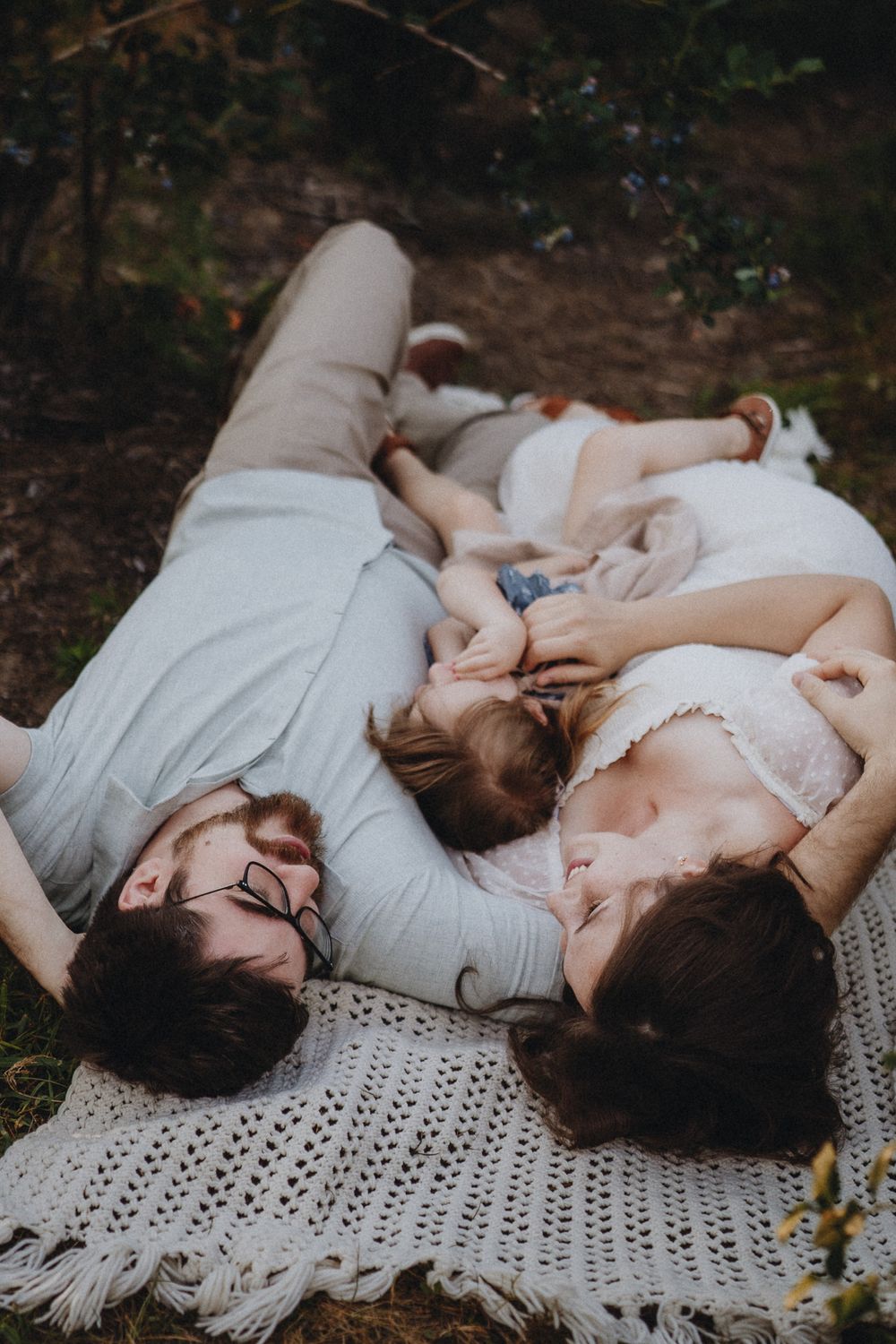 Family lying together on crochet blanket in outdoor setting.