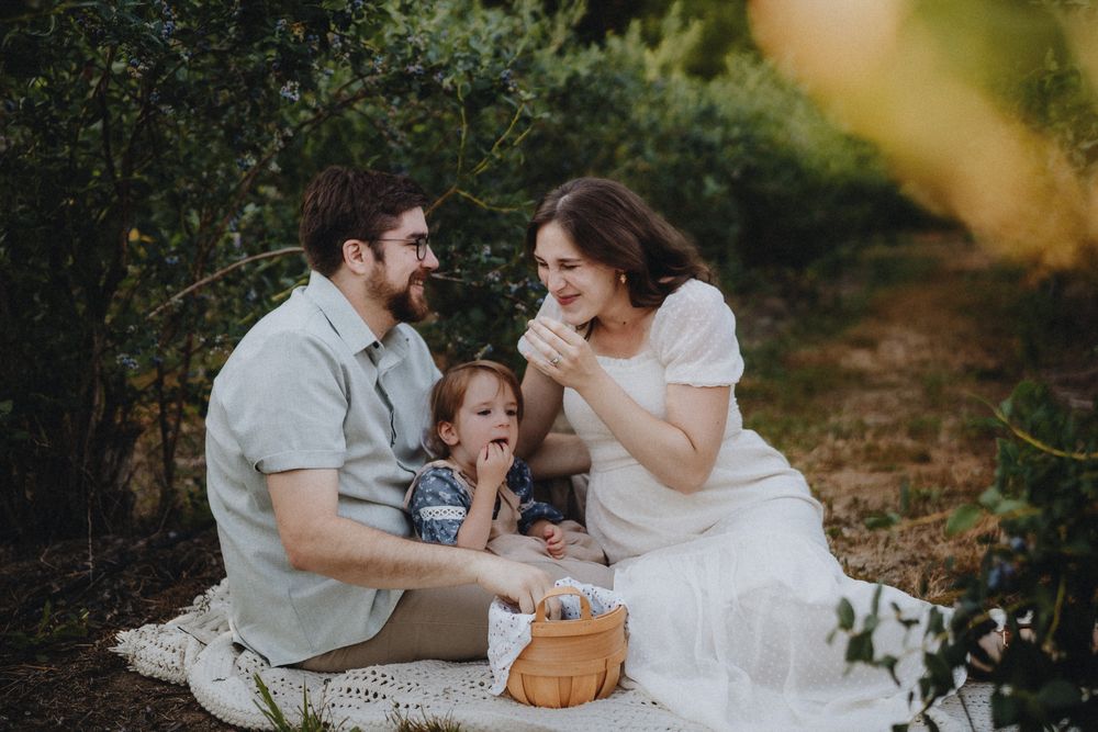 A family shares tender moments together while sitting on a white blanket in a wooded outdoor setting.