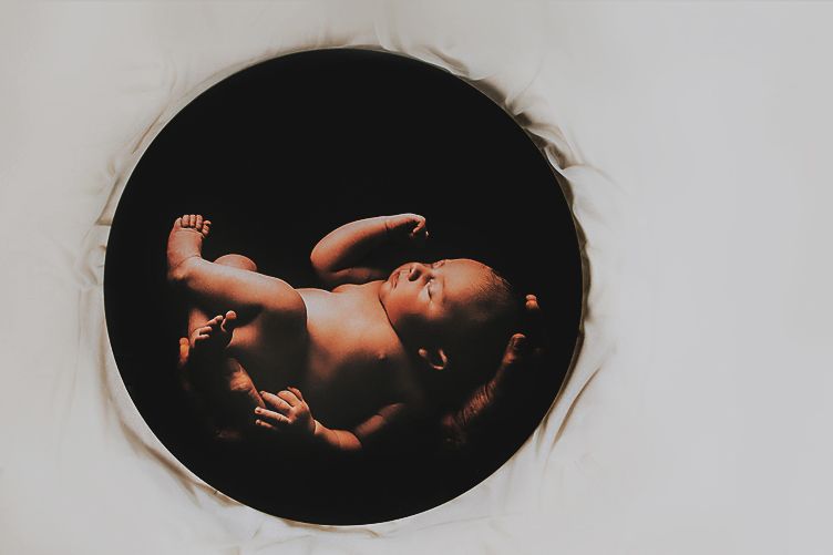 Artistic black and white photograph of a newborn baby in dramatic lighting.