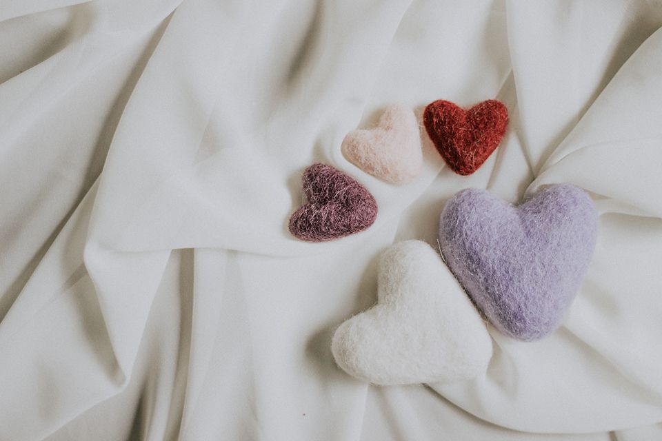 A collage of heart-shaped bath bombs in pastel colors arranged on a white fabric background.