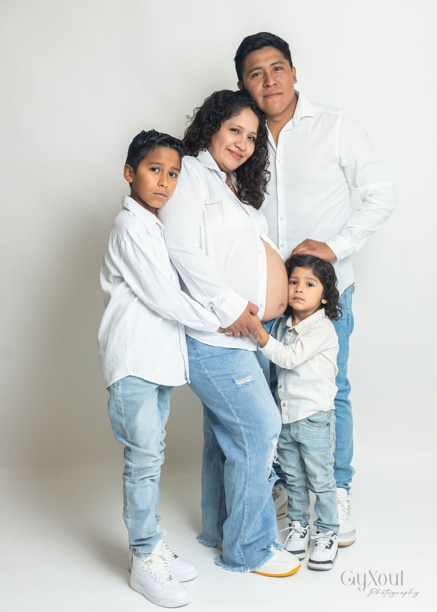 A family in matching white tops and light denim poses together against a white background in a studio setting.