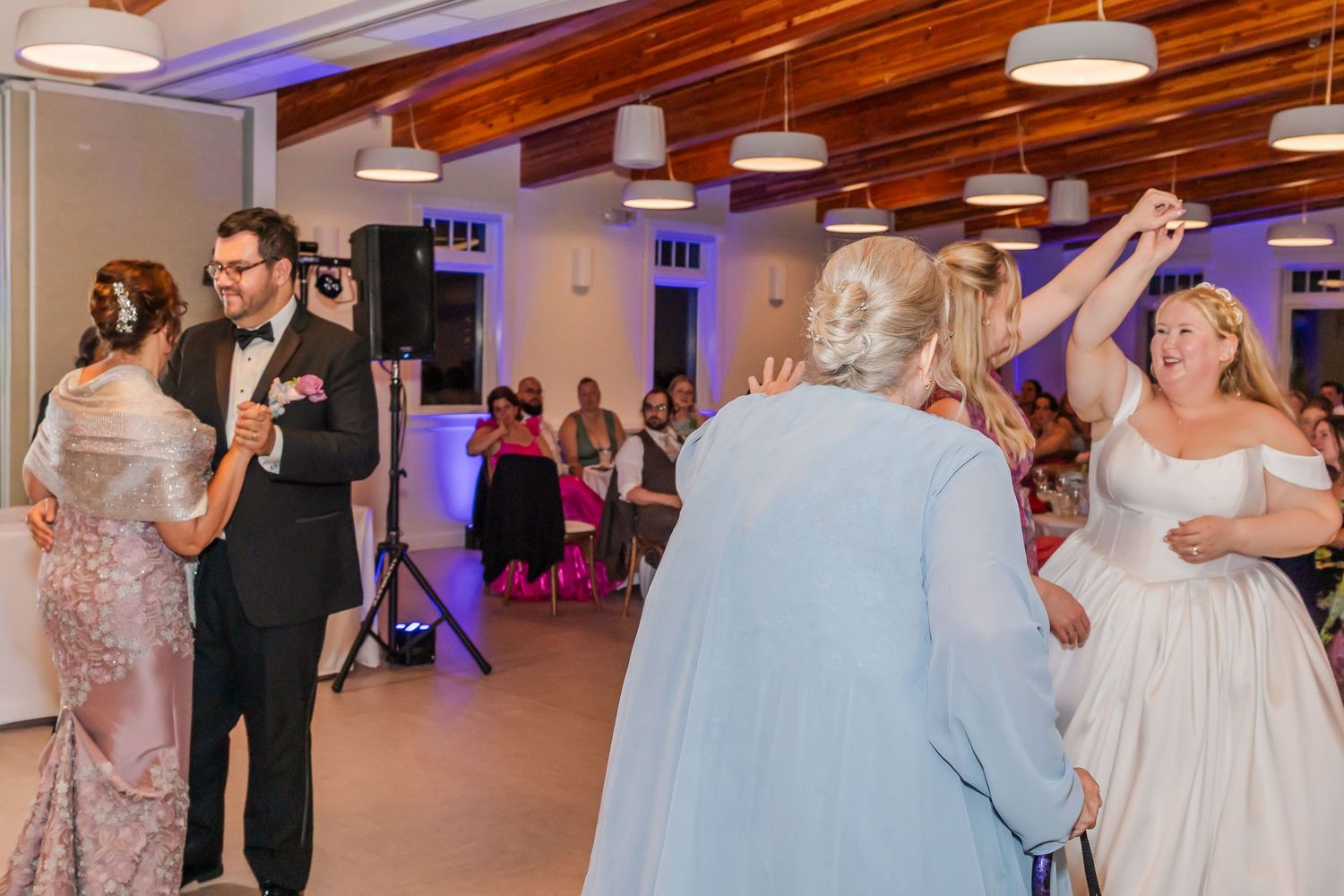 Wedding guests dance together on a large dance floor under pendant lights during an evening reception celebration.