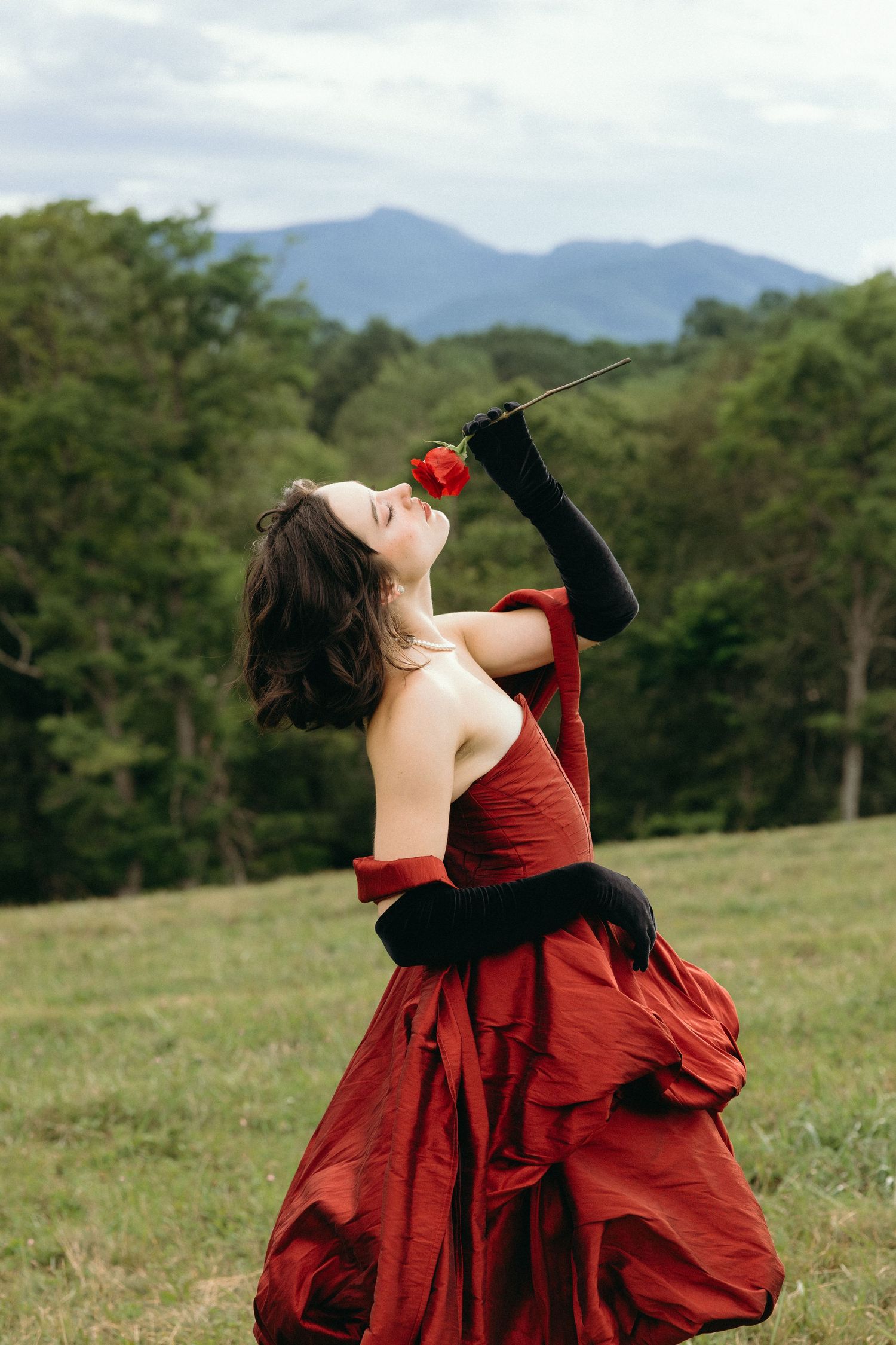 A figure in a flowing red dress twirls gracefully in a grassy meadow with mountains in the background. East Coast Luxury wedding photography