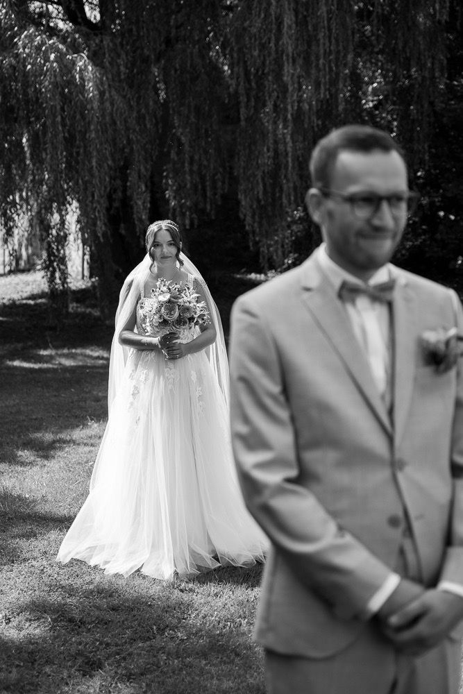 Black and white wedding photos showing a couple's first look moment under willow trees.