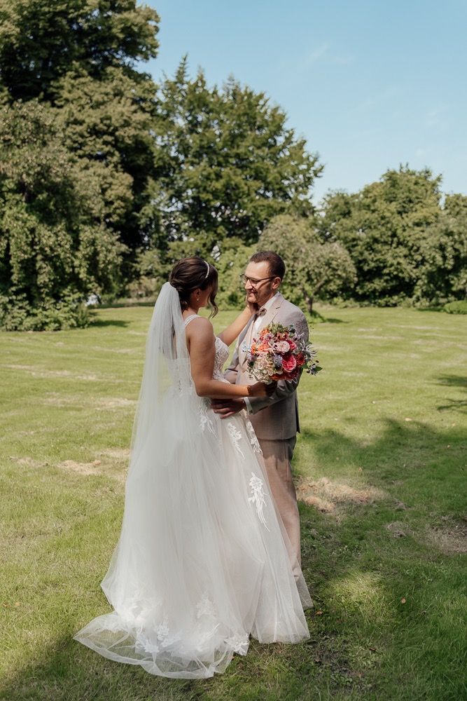A romantic wedding first look moment captured in a lush green field on a sunny summer day.