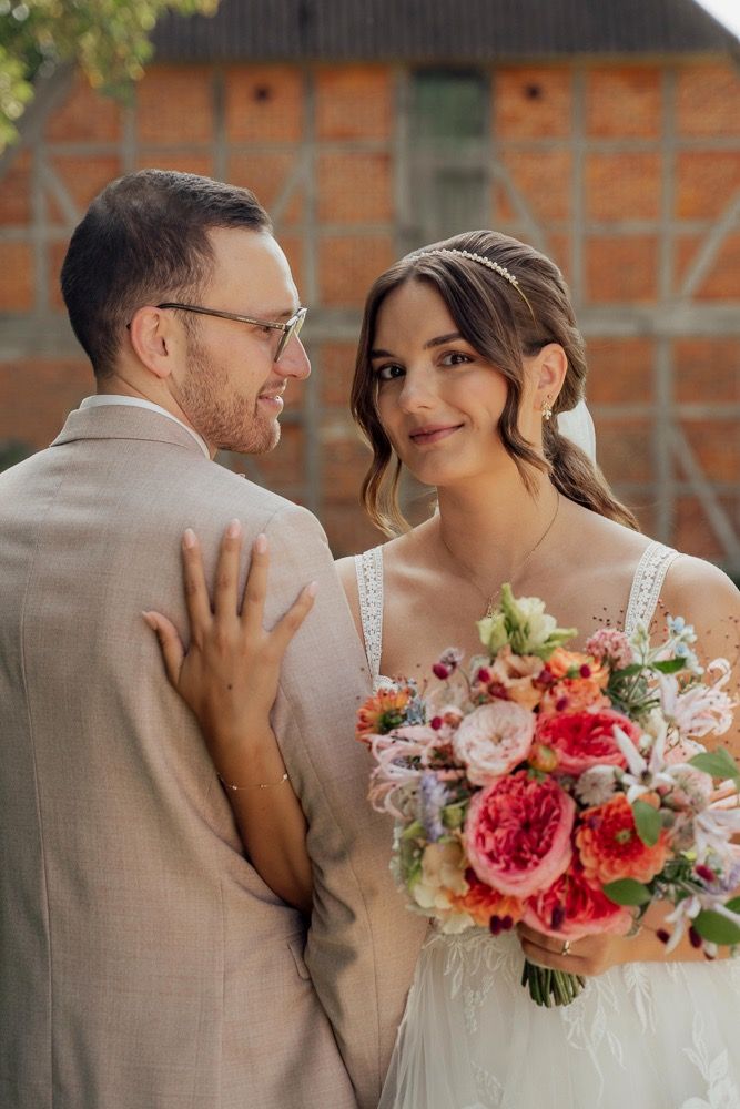 Newlyweds share tender moments while bride holds vibrant coral and pink floral bouquet.