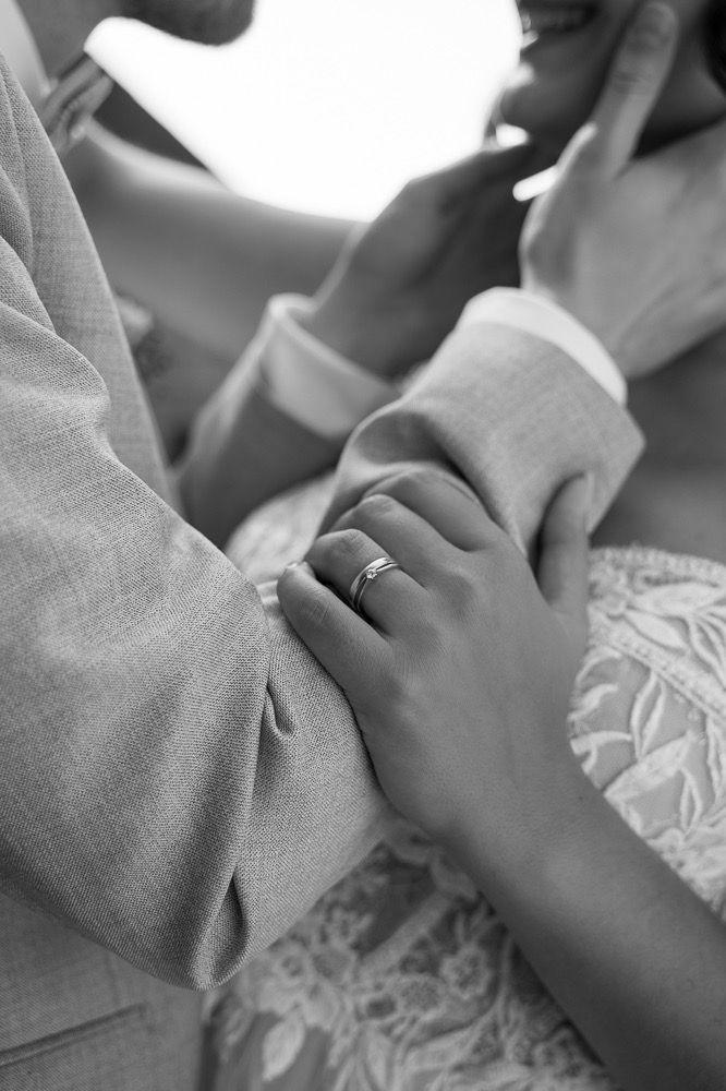 Close-up black and white photo of hands holding and caressing a small baby's hand with delicate lace fabric in frame.