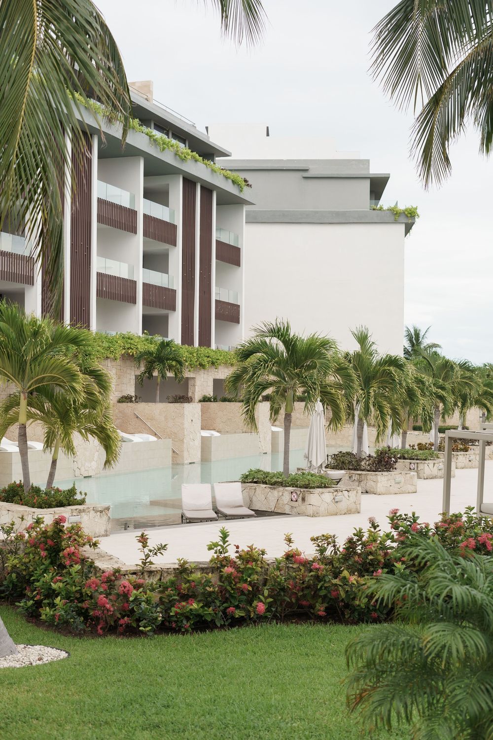 Luxury resort exterior with tropical landscaping featuring palm trees and a pool surrounded by lush gardens.