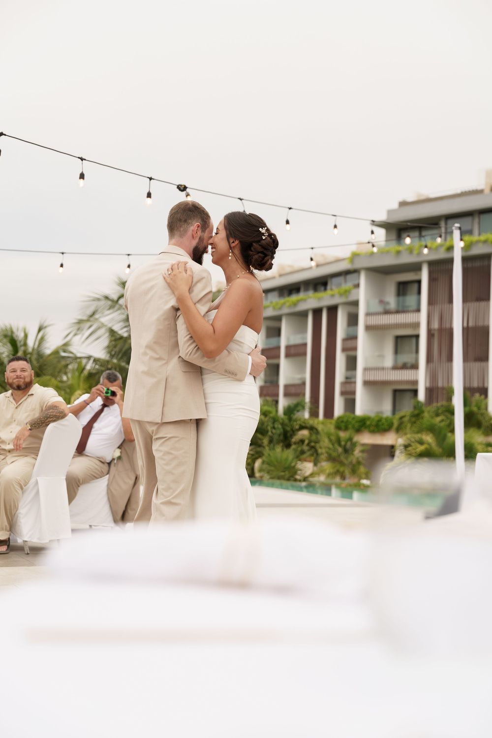 Wedding reception dance scene at a tropical venue with string lights and palm trees.