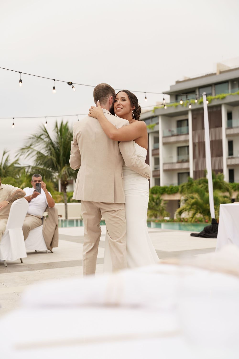 Wedding couple sharing a romantic moment on an outdoor terrace with string lights and palm trees.