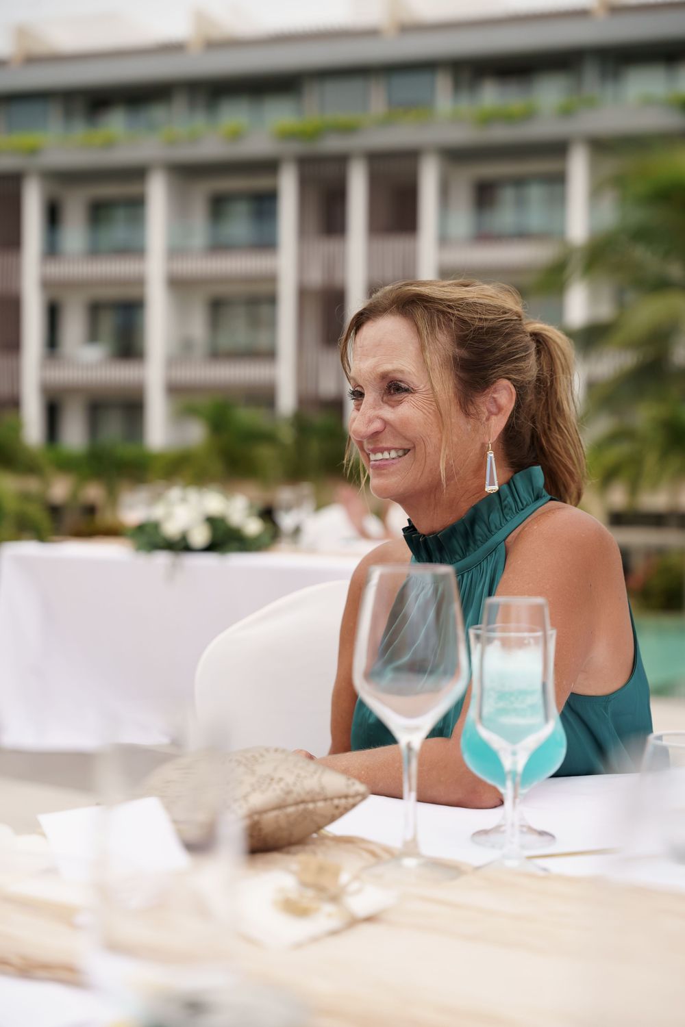 Wedding guest in teal dress enjoying reception dinner at outdoor venue.