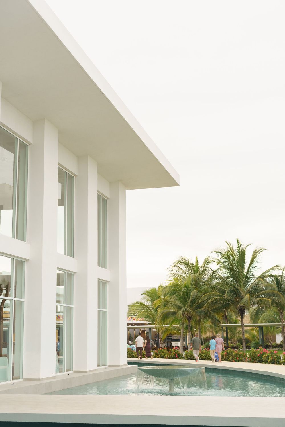 Modern white architectural building with sleek columns and a luxurious infinity pool surrounded by tropical palm trees.