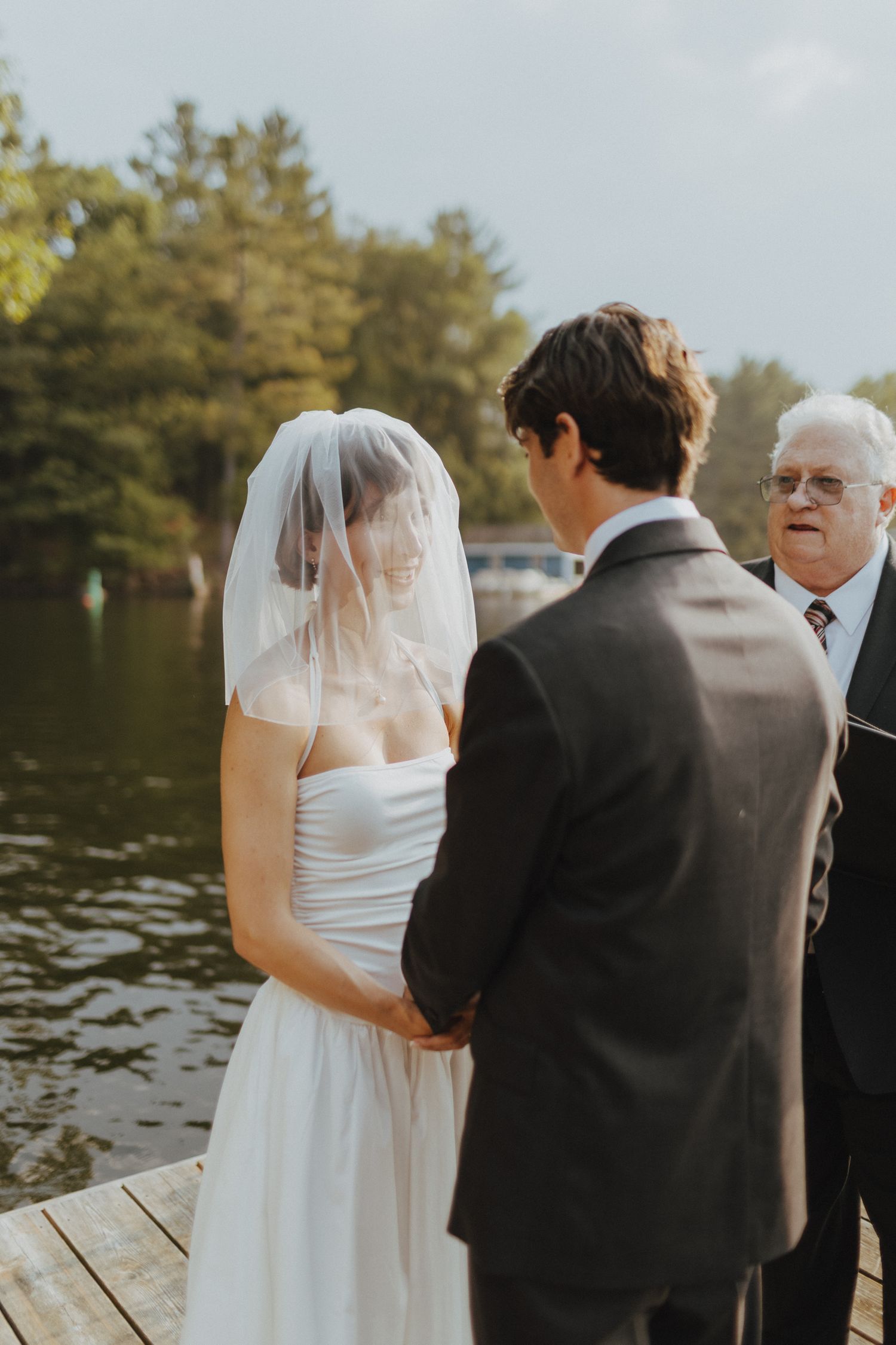 A wedding ceremony takes place on a wooden dock by a serene lake.