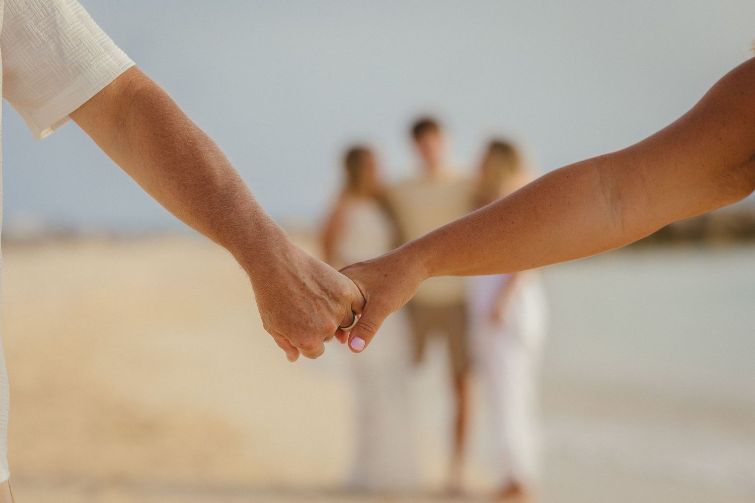 Close-up of hands reaching towards each other on a sandy beach.