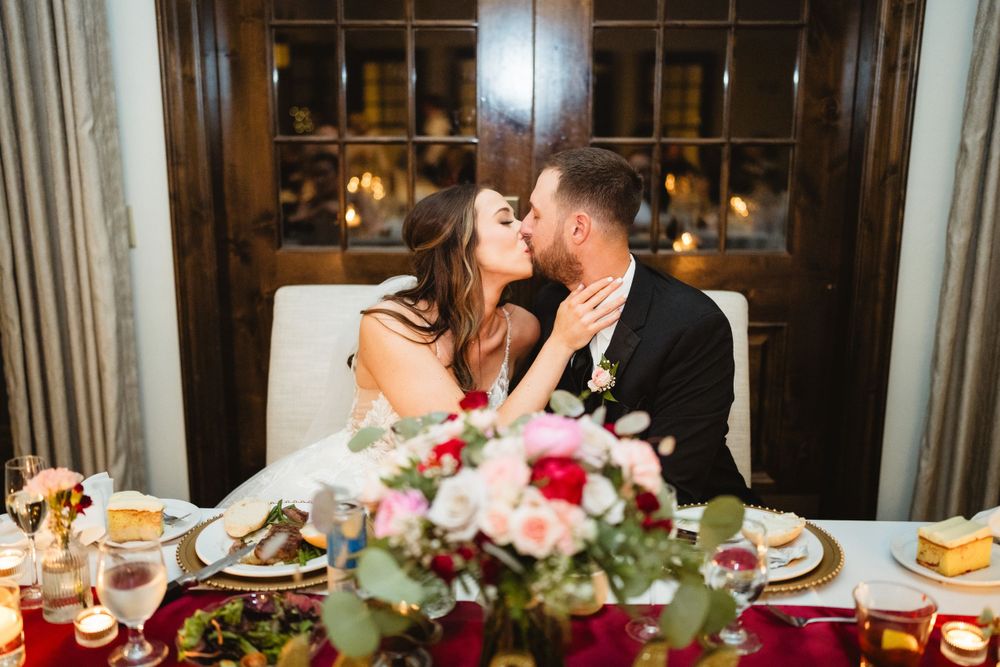 Romantic couple shares intimate moment at decorated wedding reception dinner table.