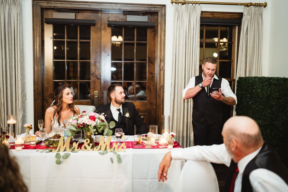 Wedding reception scene with guests seated at head table while speaker gives toast.