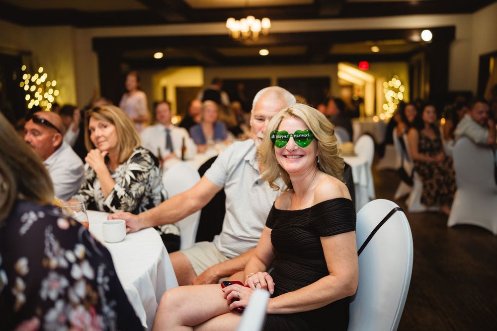 Wedding guest wearing green sunglasses enjoys festive reception atmosphere.