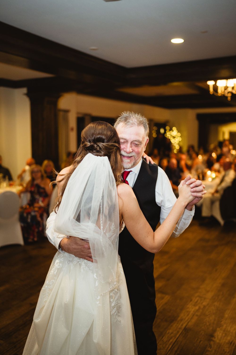 Couple shares emotional dance together during wedding reception on wooden dance floor.