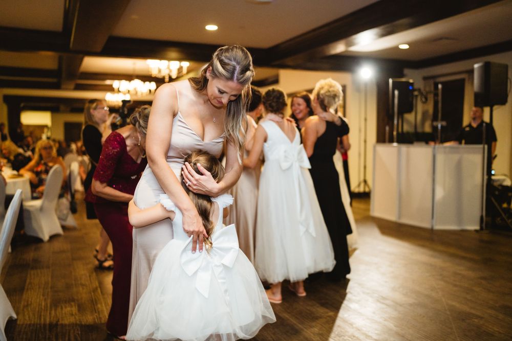 People dancing and celebrating at an indoor wedding reception with wooden floors and elegant lighting.